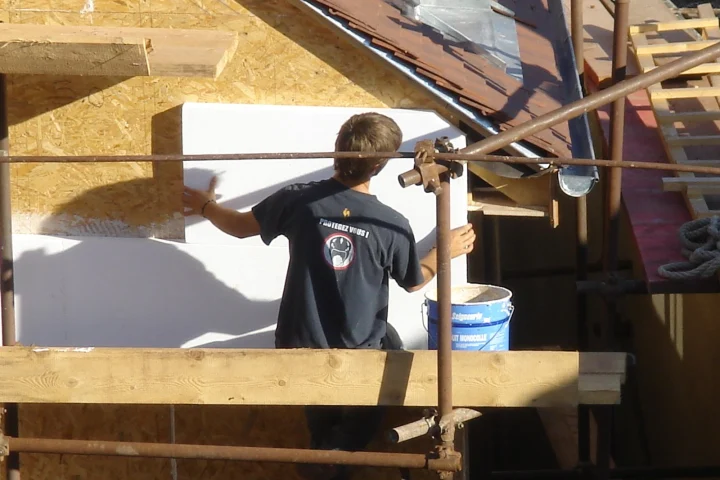 Chantier d’une maison neuve : des ouvriers posent l’isolation sur la façade à ossature bois, au stade où la dommages-ouvrage doit déjà être souscrite