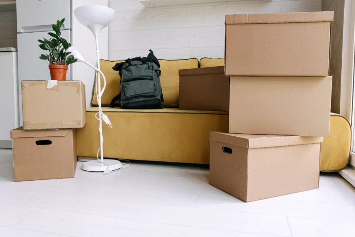 Cartons de déménagement empilés dans un salon avec canapé, lampadaire et sac à dos