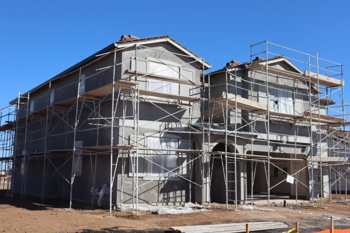 Maison à étage en construction, entourée d’échafaudages sous un ciel bleu