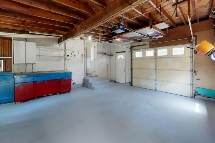 Garage vide au sol peint en gris clair, avec un établi bleu et rouge et une porte sectionnelle au fond