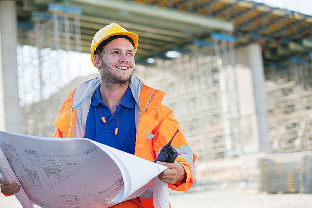 Constructeur en tenue de chantier qui tient un plan de construction